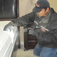 Bed bug inspection technician checking a mattress and bed frame for signs of infestation in Boca Raton, FL