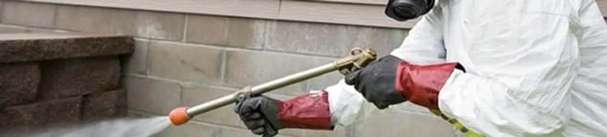 Pest control technician applying exterior insect treatment along a home foundation in Boca Raton, FL