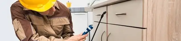 Roach exterminator applying treatment under kitchen cabinets in Boca Raton, FL