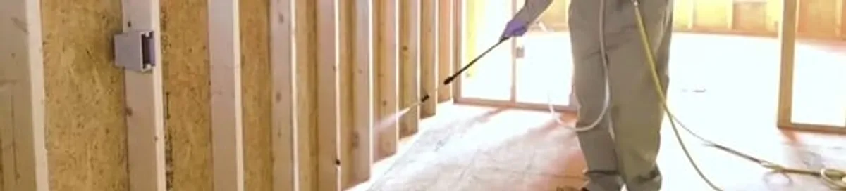 Termite treatment technician applying spray along framing and unfinished walls in Boca Raton, FL