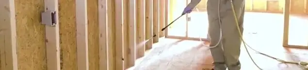 Termite treatment technician applying spray along framing and unfinished walls in Boca Raton, FL